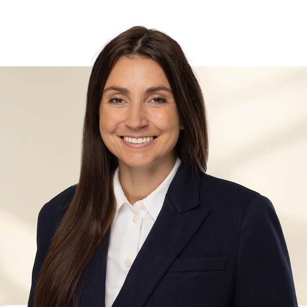 Porträt von Alexandra Meyer mit langen, glatten, dunkelbraunen Haaren, weissem Hemd und dunkelblauem Blazer vor neutralem, unscharfem Hintergrund