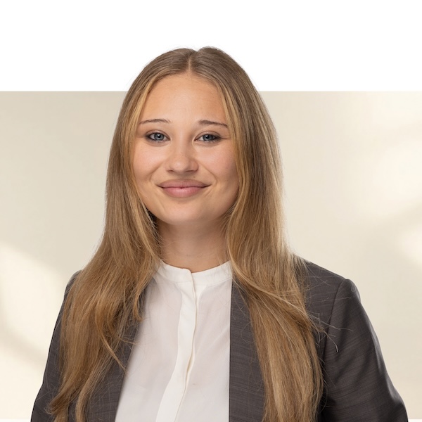 Porträt von Giada Stadler mit langen, glatten, blonden Haaren, weisser Bluse und dunklem Blazer vor neutralem, unscharfem Hintergrund